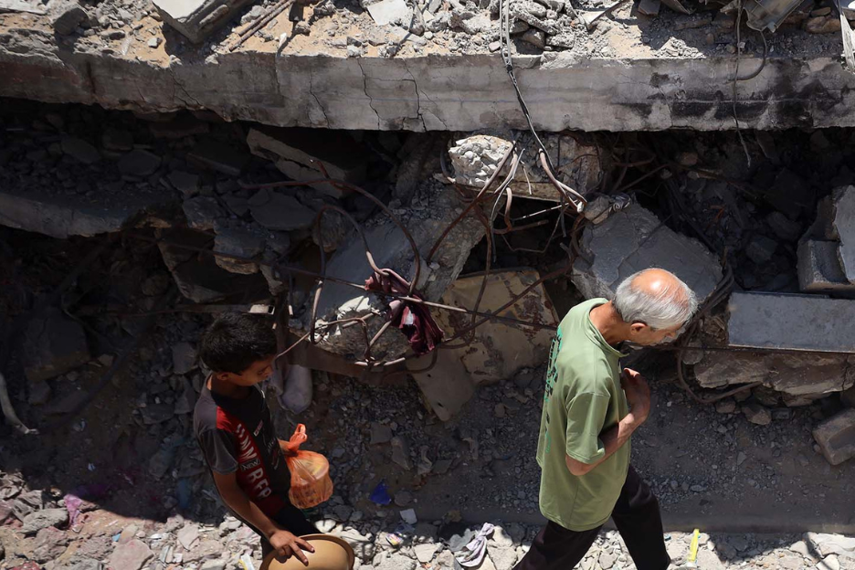 Ein Junge und ein älterer Mann gehen in gebeugter Haltung an einer Ruine vorbei.